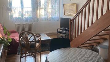 Una sala de estar acogedora con una escalera de madera, una mesa de comedor con mantel estampado, un televisor y un radiador.