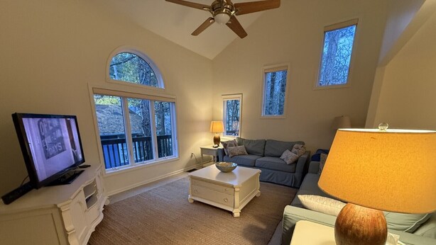 A living room with a television, a sofa, a coffee table, and a lamp. There are windows and a ceiling fan. - Spacious 5-bedroom house in adorable Bethany Beach with AC (Bethany Beach)