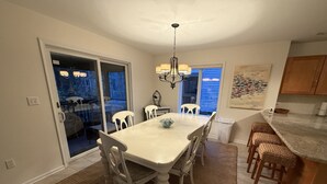 A dining area with a table and chairs, a chandelier, a kitchen with bar stools, and a view through a glass door. - Spacious 5-bedroom house in adorable Bethany Beach with AC (Bethany Beach)