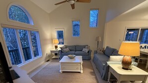 A spacious living room with a large window, a ceiling fan, and a cozy seating area. - Spacious 5-bedroom house in adorable Bethany Beach with AC (Bethany Beach)