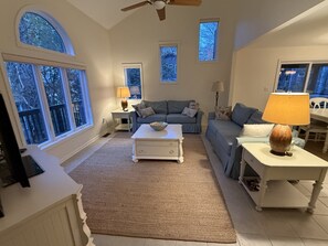 A spacious living room with a large window, a ceiling fan, and a cozy seating area. - Spacious 5-bedroom house in adorable Bethany Beach with AC (Bethany Beach)
