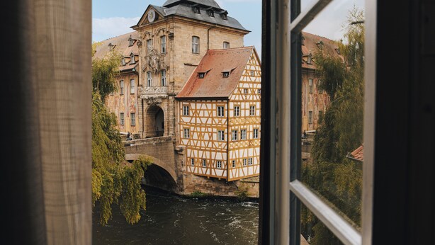A historic building with a prominent tower and a bridge over a river. - HOY bamberg boutique hotel (Bamberg)
