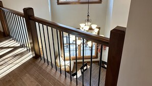 A wooden staircase with a railing leading to a dining area with a chandelier. - Luxury, Modern 4 Bedroom House with Full Basketball and Pickleball Courts! (Old Forge)