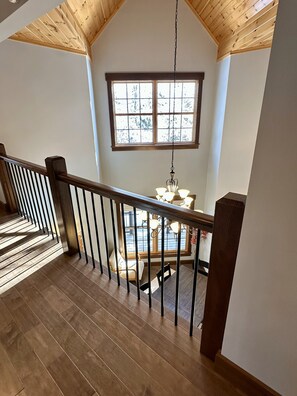 Un escalier en bois, doté d’une rampe, mène à une salle à manger agrémentée d’un lustre.