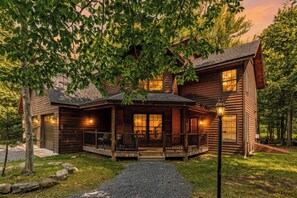 Une cabane en rondins avec un porche, de grandes fenêtres et une allée gravillonnée.