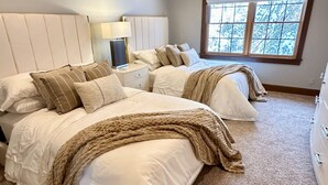 A bedroom with two beds, a ceiling fan, a window with a view of trees, and a nightstand with a lamp. - Luxury, Modern 4 Bedroom House with Full Basketball and Pickleball Courts! (Old Forge)