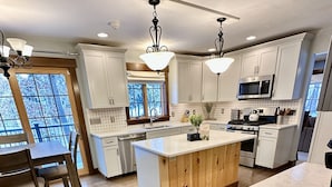 A modern kitchen with white cabinets, a wooden island, stainless steel appliances, and a large window. - Luxury, Modern 4 Bedroom House with Full Basketball and Pickleball Courts! (Old Forge)