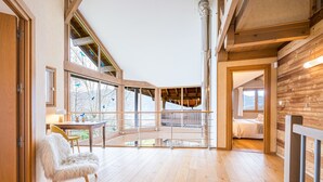 Une pièce spacieuse avec un plancher en bois, un fauteuil blanc et moelleux, une table et un lit.