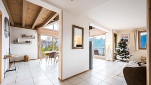 Un vaste espace de vie doté d’un plafond en bois, d’une table à manger, de chaises, d’un sapin de Noël et offrant une vue sur l’extérieur.