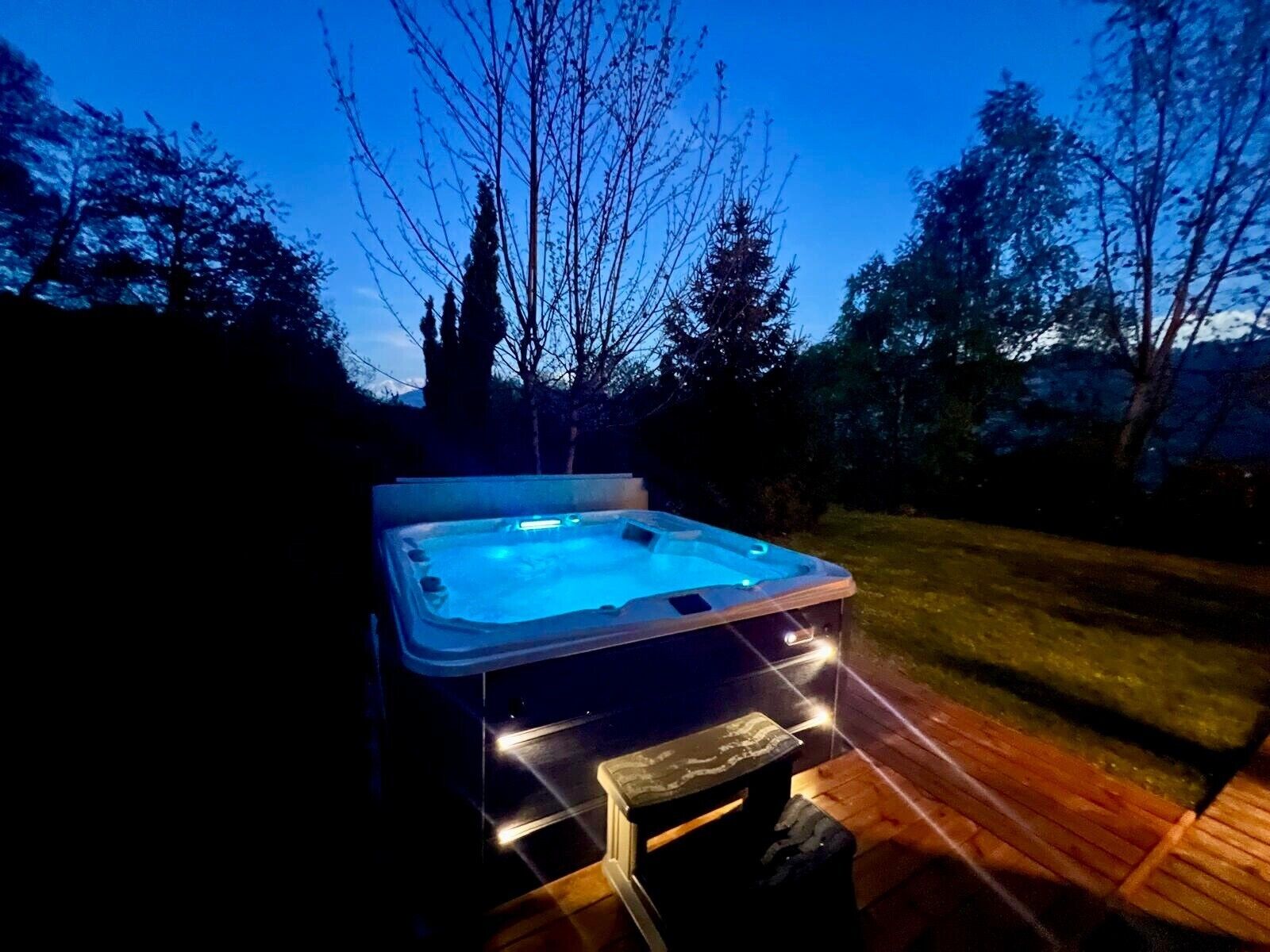A hot tub with a wooden deck and a stone bench, surrounded by trees.
