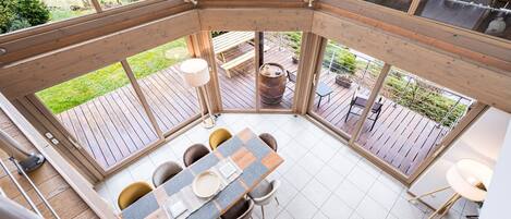 Une pièce d’angle dotée d’une terrasse en bois, d’une table à manger avec des chaises et donnant sur le jardin.