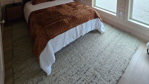 Ein Schlafzimmer mit Holzbalkendecke, einem Bett mit brauner Steppdecke, zwei Nachttischen und einem großen Fenster.
