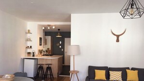 Een knus woongedeelte met een keukenhoek, een eettafel, een bank met kussens en een lamp.