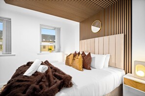 Ein modernes Schlafzimmer mit einem großen Bett, einem Holzkopfstück und einem Nachttisch mit einer Lampe.