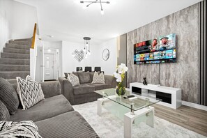 Ein modernes Wohnzimmer mit Treppe, einem großen Flachbildfernseher und minimalistischem Design.