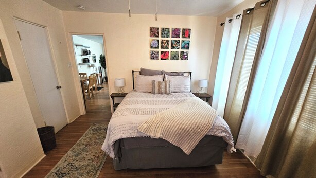Une chambre à coucher avec un grand lit, une table de chevet, une lampe, un mur orné de tableaux encadrés et une fenêtre avec des rideaux.