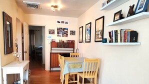 Un coin repas accueillant avec une table et des chaises en bois, une console blanche ornée d’un vase et une bibliothèque remplie de livres et de photos encadrées.