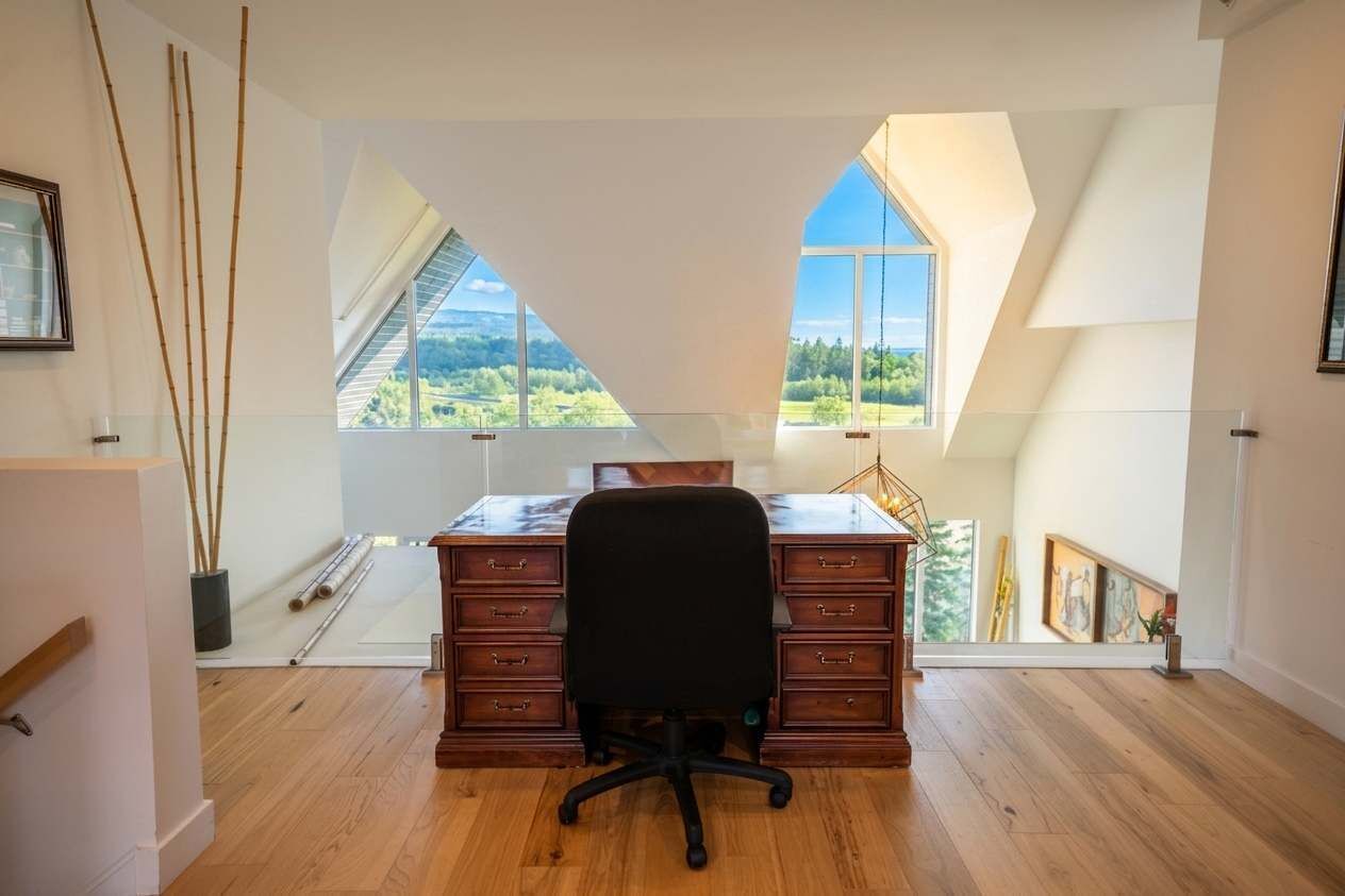 Una habitación amplia con un escritorio grande, piso de madera y vista a un paisaje a través de un tragaluz.