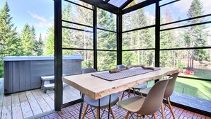 Eine überdachte Terrasse mit einem Holztisch und -stühlen, einem Whirlpool und Blick auf einen Wald.