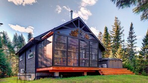 Eine moderne Holzhütte mit großen Fenstern, einem geneigten Dach und einer Holzterrasse.