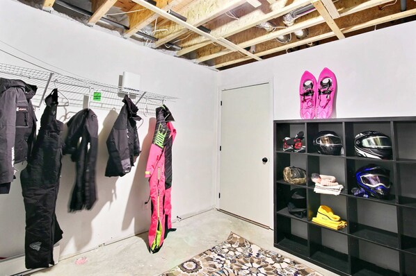 A room with a wooden ceiling, a black shelving unit with helmets and a pair of pink shoes, and a wall with hanging jackets. - Spa - Waterfront | Le NördikA (Shannon)