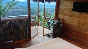 Un dormitorio con una cama grande, piso y pared de madera, televisor y balcón con vistas al paisaje.