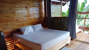 Una cama con estructura de madera y ropa de cama blanca en una habitación con paredes y suelos de madera.