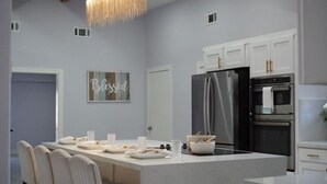 Een moderne keuken met een groot kookeiland, roestvrijstalen apparatuur en een bordje met de tekst 'Blessed'.