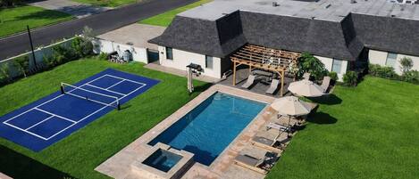 A residential property with a swimming pool, tennis court, and a covered patio area.