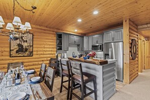 Interno di una baita in legno con zona pranzo, cucina e un'ampia porta di legno.