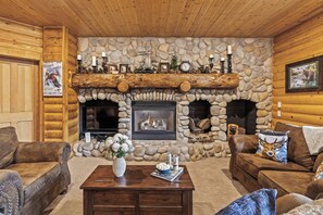 Interno di una baita di legno con camino in pietra, mobili in pelle e televisore.