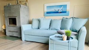 A living room with a sofa, a small table with a plant, a painting of a sailboat, and a stone fireplace. - Lake House on the Shores of Möhnesee (Möhnesee)