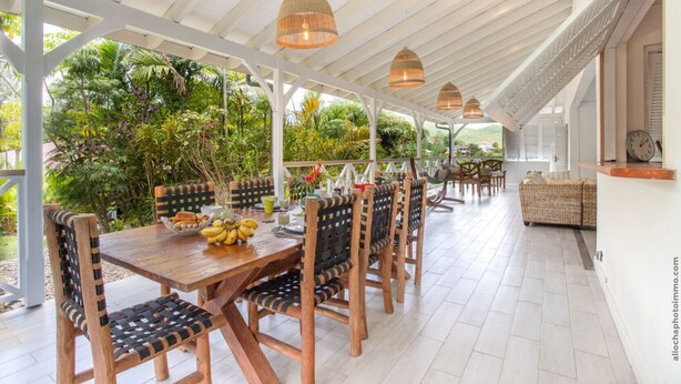 A covered outdoor dining area with wooden tables and chairs, surrounded by lush greenery. - Alizéa (Le Diamant)