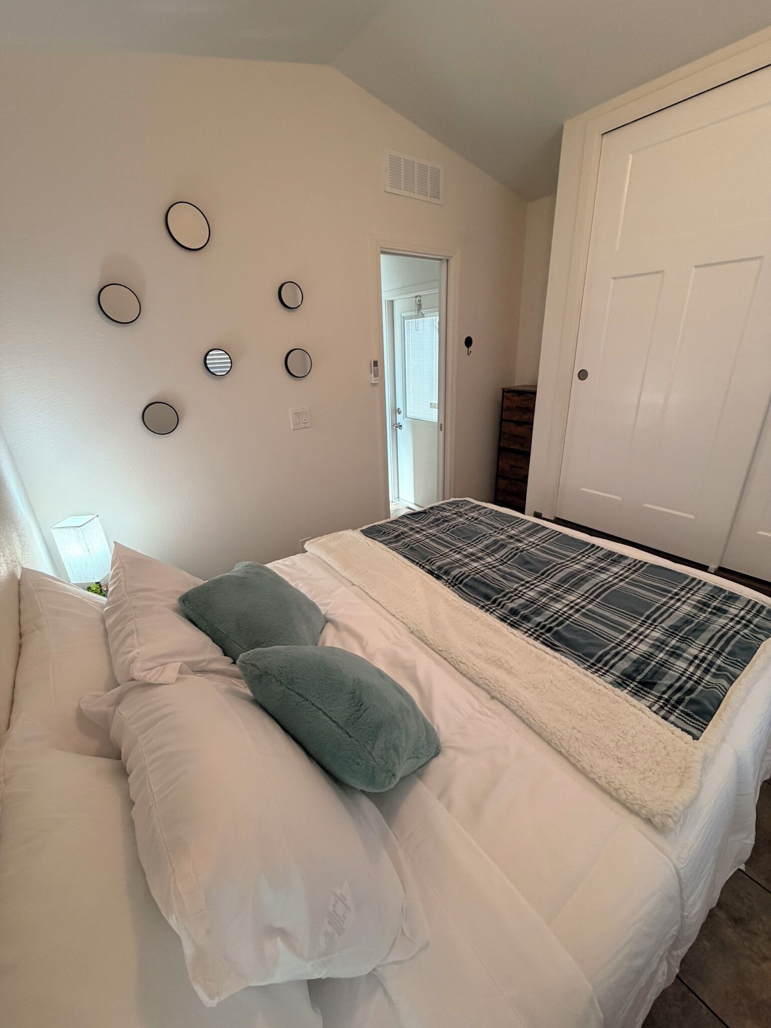 Un dormitorio con cama, almohadas, una puerta y espejos circulares fijados a la pared.