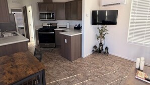 Una cocina moderna con una isla central, microondas integrado y electrodomésticos de acero inoxidable. Hay una zona de comedor con una mesa y sillas de madera.