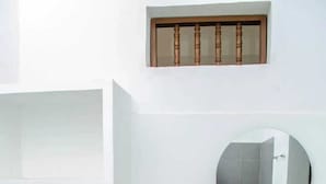 A bathroom with a toilet, a round mirror, a sink, and a wooden cabinet. - SGH SAN AGUSTIN HOTEL (Santa Marta)