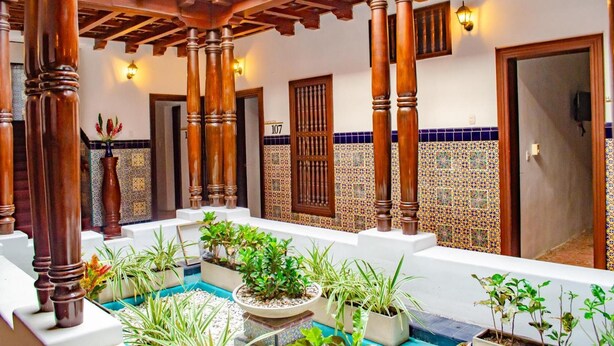 A courtyard with a pool, potted plants, wooden pillars, and tiled walls. - SGH SAN AGUSTIN HOTEL (Santa Marta)