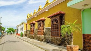 A street view of a row of yellow buildings with stone walls and wooden window shutters. - SGH SAN AGUSTIN HOTEL (Santa Marta)