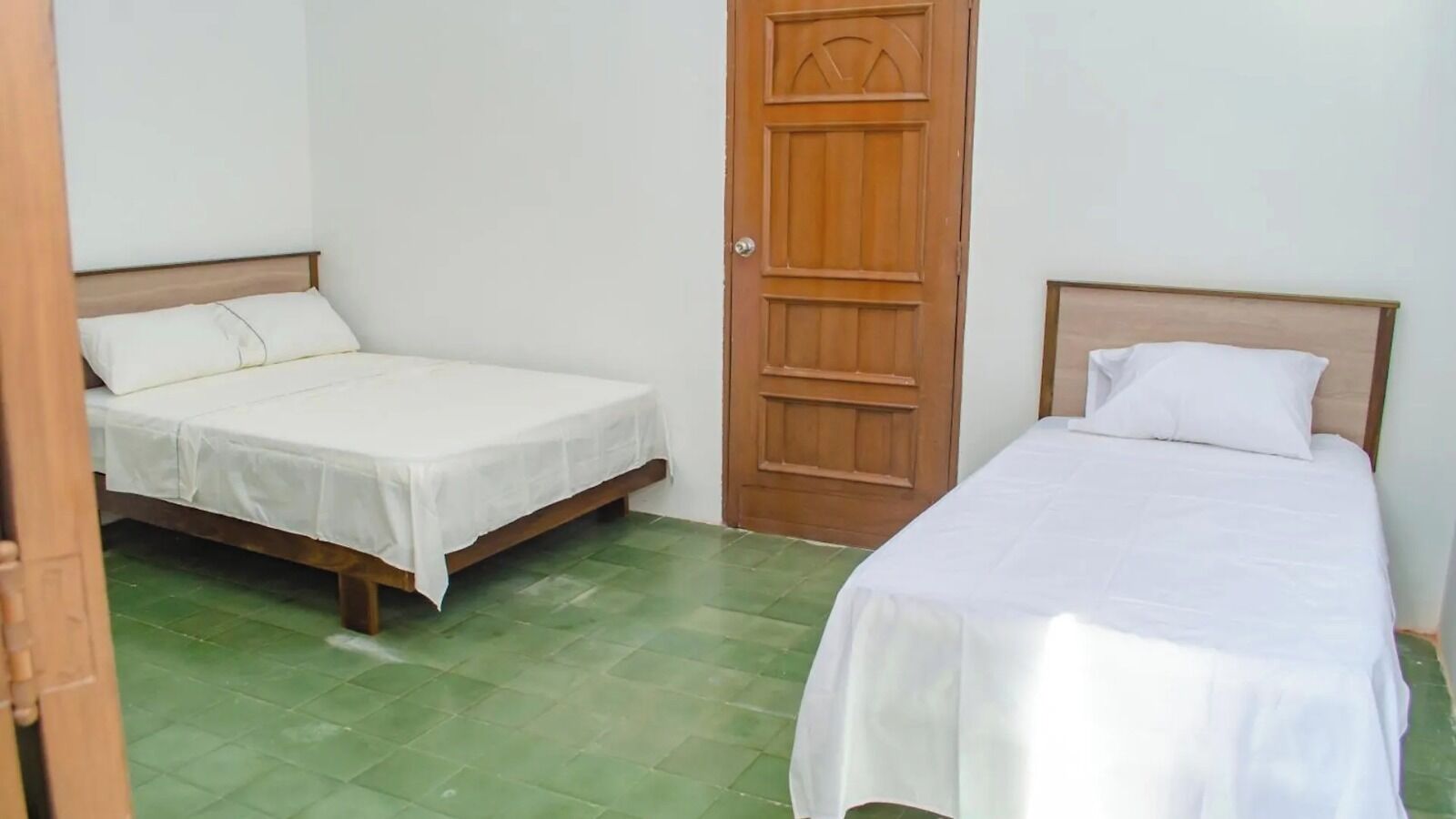 A room with two single beds, a wooden door, and green tiled flooring.