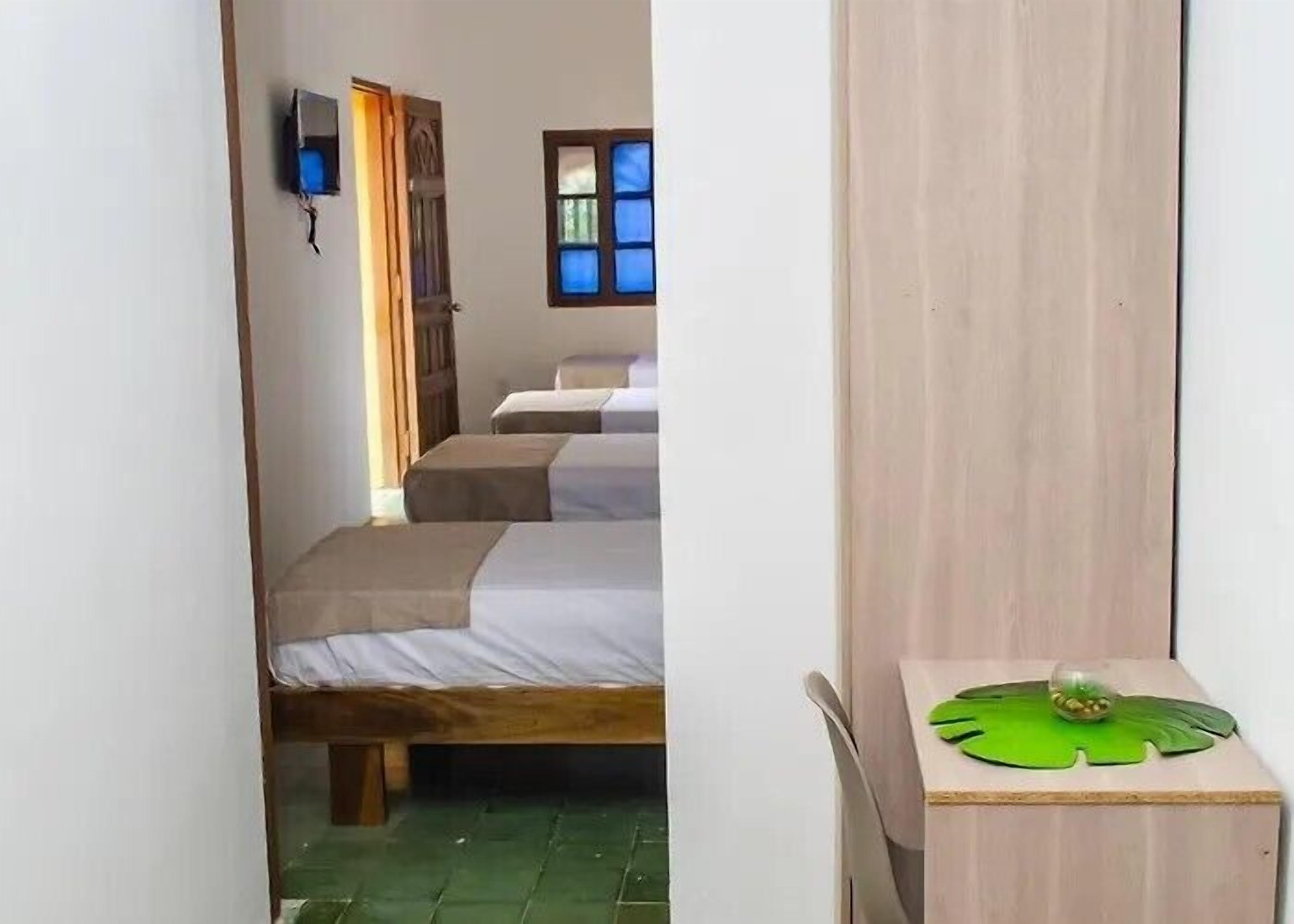 A room with two beds, a wooden table with a green leaf design, and a window with blue-tinted glass.