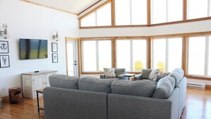Un salon moderne avec un canapé d’angle, un téléviseur à écran plat et de grandes fenêtres.