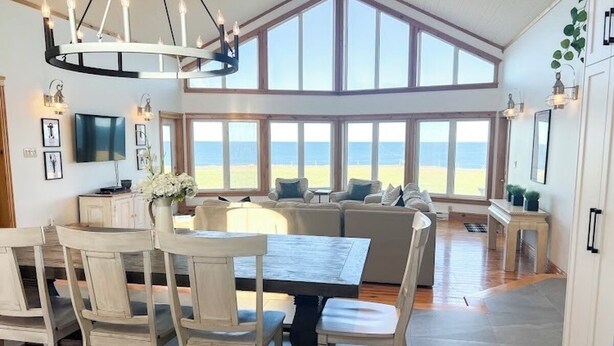 Un vaste espace de vie avec une grande fenêtre donnant sur la plage, une table à manger avec des chaises et un lustre moderne.