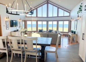 Un vaste espace de vie avec une grande fenêtre donnant sur la plage, une table à manger avec des chaises et un lustre moderne.