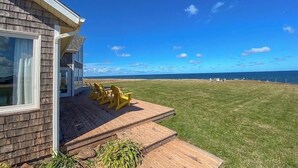 Une maison avec une terrasse et des chaises, une pelouse verdoyante et une vue sur l’océan.