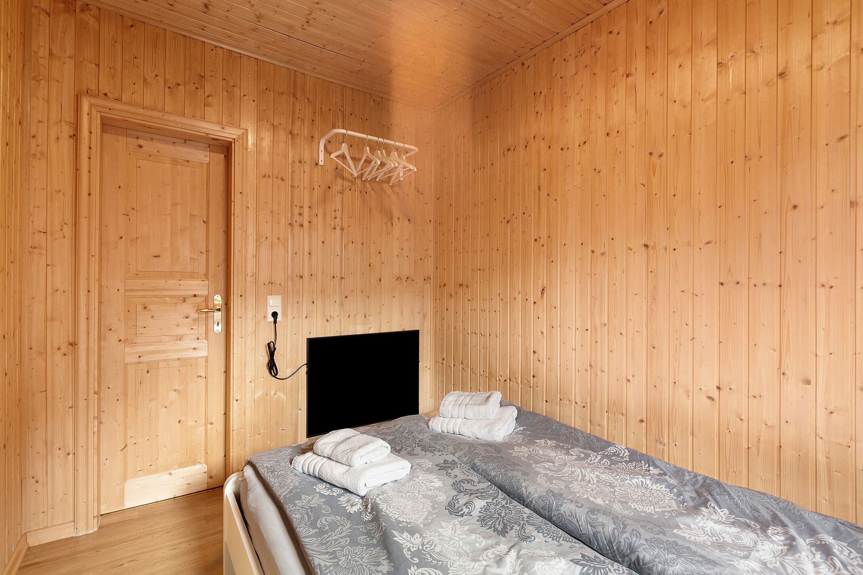 A wooden-paneled room with a bed, a door, and a wall-mounted light fixture.