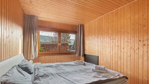 Une pièce aux murs lambrissés, avec un lit, une fenêtre et des rideaux.