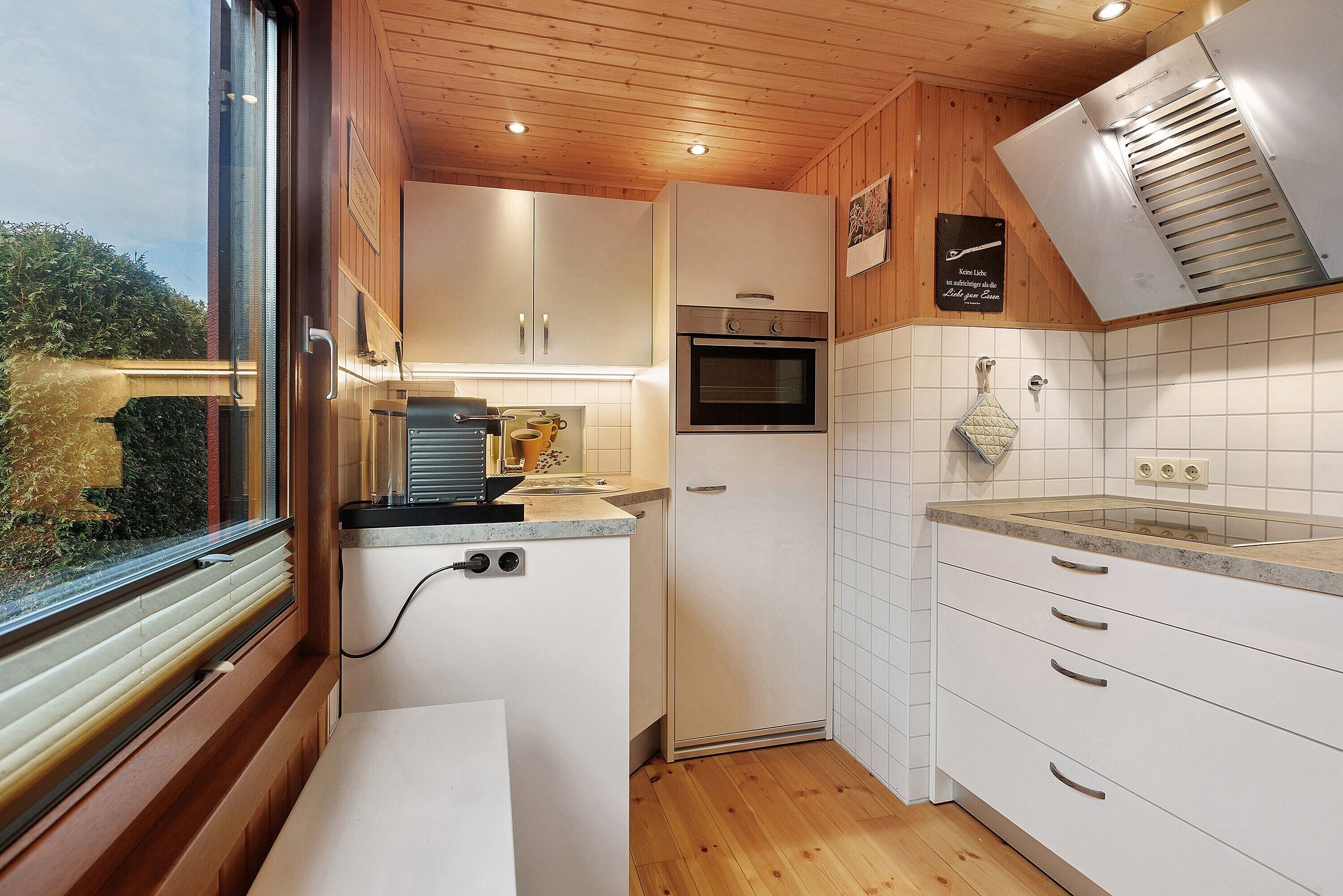 Eine moderne Küche mit Holzausstattung, einem Einbauofen und einem Fenster mit Blick auf Grünflächen.