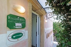 Ein Gebäudeeingang mit einem grünen Schild für 'Rosadi Mare Gorra Finale Ligure Rooms' und einem schlüssel-förmigen Emblem für 'AFFITTACAMERE'.