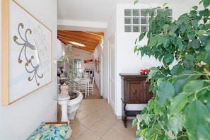 A hallway with a white tiled floor, a white pedestal table with a pink lantern, a wooden cabinet, and a large green plant. - 'Peperoncino' Room with Hill View (finale ligure)