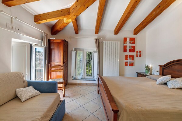 A bedroom with a wooden ceiling, a bed, a sofa, a window, and a door.
